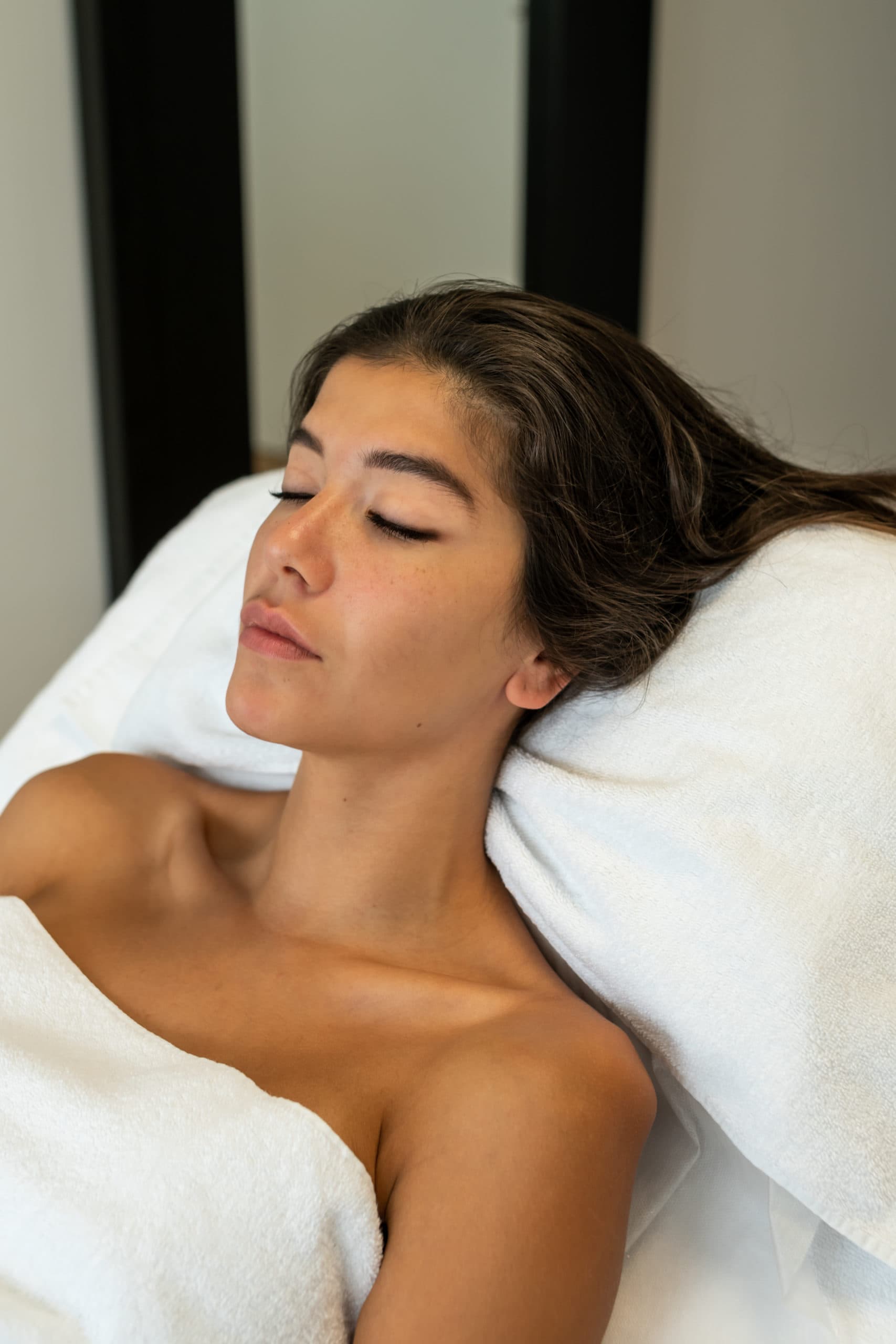 Une femme brune allongée sur un siège de soin blanc.